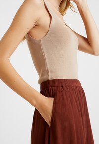 Beige ribbad linne i kombination med en flödande kjol i rostfärg med en rynkad midja och sidofickor. Tygkvaliteten är jämn och designen är avslappnad.