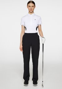 Vit pikétröja med korta ärmar och svarta detaljer, ihop med svarta byxor. Inkluderar golfhandske och klubba. Slank, sportig design.