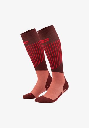 Kompressionsstrümpfe in Braun und Pink, mit vertikalen roten Streifen und einem Logo. Hergestellt aus strukturiertem Material, entworfen für Komfort und Unterstützung.