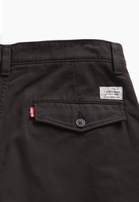 Poche arrière d'un pantalon noir Levi's avec rabat à bouton, étiquette rouge Levi's et étiquette de marque blanche Levi Strauss of California.