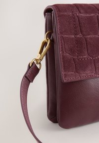 Burgundy handbag with a textured suede front, smooth leather sides, gold hardware, and a detachable strap. Features a flap closure.
