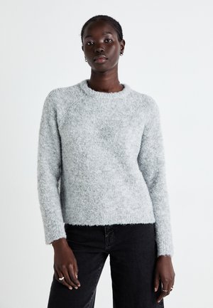 Pull en peluche gris clair avec un col rond, des manches longues et une coupe décontractée. La texture du tissu est douce et légèrement côtelée en bas.