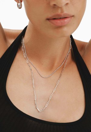 Collares de plata con una fina cadena y un diseño de clip de papel más grande. Llevados sobre una camiseta negra, destacando las texturas metálicas elegantes.