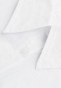 Biała bawełniana koszula z kołnierzem typu spread, dwoma guzikami i widocznymi detalami przeszyć. Gładka faktura, bez wzorów i ozdób.