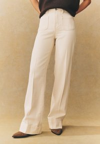 Pantalon ample couleur crème en coton avec une taille haute, doté de passants pour ceinture, deux poches avant et un revers discret à l'ourlet.