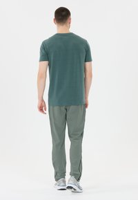 Groene T-shirt met korte mouwen en lichtgrijze sportsbroeken, met een gladde textuur en slim fit, gezien van achteren.