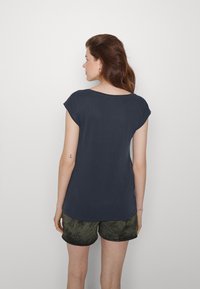 Camisa de manga curta azul-marinho com um ajuste descontraído e decote redondo, combinada com calções em camuflagem verde-escuro. Textura suave, design simples.