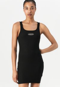 Čierne rebrové šaty bez rukávov s priliehavým strihom. Obsahujú výstrih do oválu a logo na hrudníku. Mäkka textura a elastický materiál.