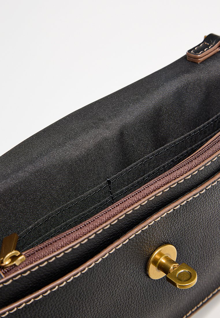 Sac à main en cuir noir avec une fermeture à bouton doré, des coutures marron et un intérieur spacieux doublé de tissu noir lisse.