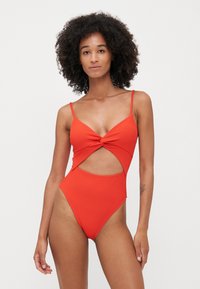 Maillot de bain une pièce rouge à côtes avec un devant torsadé, détail découpé sur le côté et fines bretelles réglables. Texture lisse, échancrure haute.
