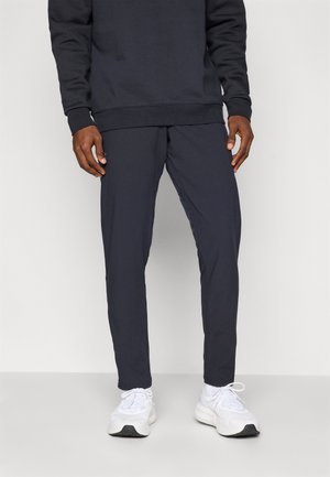 Navy sweatpants with a relaxed fit, elastic waistband, and side pockets. Paired with white athletic shoes featuring textured soles.