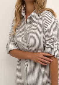 Koszula z guzikami, w pionowe czarne i białe paski, z kołnierzykiem, rękawami typu roll-up i luźnym krojem. Teksturowana tkanina.