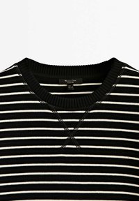 Pull à rayures noires et blanches avec col ras du cou côtelé et détail décoratif en point de V au centre avant.