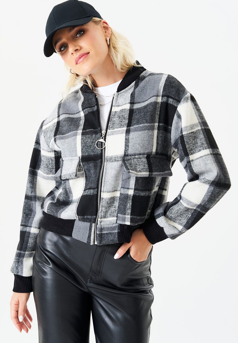 Black and white plaid bomber jacket with a zip front, two chest pockets, and ribbed cuffs. Worn over black leather pants.