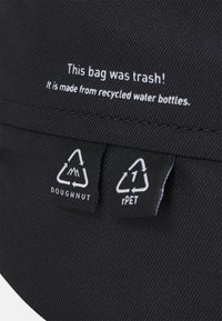 Zwarte tas gemaakt van gerecyclede waterflessen, met textuurstof en een binnenlabel met de tekst "Deze tas was vuilnis!" met recycling-symbolen.