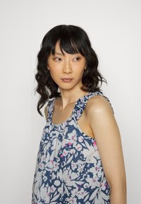 Top sem mangas com estampado floral em azul marinho e branco, com detalhes em rosa. Apresenta alças de ombro com babados e um corte solto. Tecido macio.