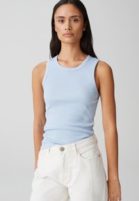 Canotta a righe blu chiaro con scollatura rotonda e spalline larghe, abbinata a jeans bianchi con chiusura a bottone e tasche laterali.