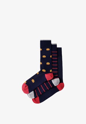 Tres pares de calcetines azul marino con punteras rojas; uno tiene caras de perro amarillas, otro rayas rojas y otro un patrón de pequeños puntos blancos.