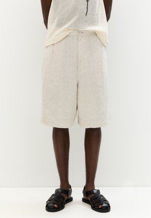 Light beige linen shorts with a relaxed fit, featuring pleats and side pockets, paired with black strappy sandals.