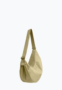 Borsa a tracolla beige con ampia tracolla regolabile e corpo curvo e morbido su uno sfondo chiaro e semplice.