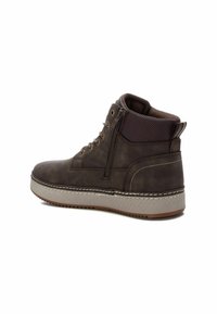 Stivali alti in pelle marrone con chiusura a zip, superficie texturizzata, suola grigia a contrasto e dettagli cuciti lungo il bordo.
