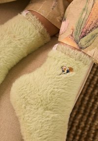 Calcetines verdes claros y difusos con una textura suave, con un diseño floral bordado y acentos brillantes en la parte superior.