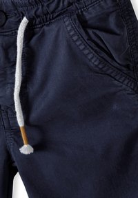 Pantaloni corti in misto cotone blu navy con vita elastica, chiusura con coulisse e tasche laterali. Tessuto a texture con un leggero lucido.