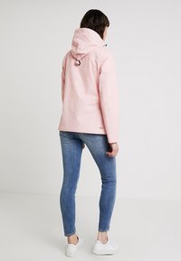 Jasnoróżowa wodoodporna kurtka z kapturem, zapinana na zamek błyskawiczny i wyposażona w regulowane sznurki, zestawiona z obcisłymi niebieskimi dżinsami i białymi trampkami.