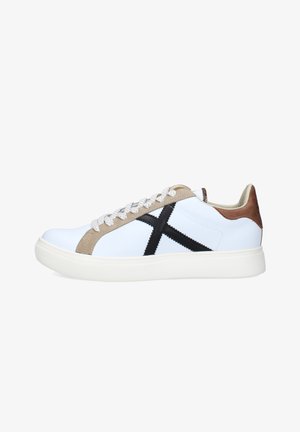 Zapatilla blanca de corte bajo con detalles en beige, "X" negra cosida en el lateral, cordones blancos, lengüeta marrón en el talón y suela blanca gruesa.