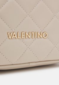 Patšįstas smėlio spalvos odinis rankinė su auksiniu "VALENTINO" logotipu. Išskirtinis įstrižinis siuvinėjimas ir lygus paviršius. Minimalistinis dizainas.