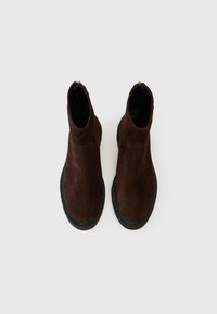 Botine din suede maron cu vârf rotund și talpă din cauciuc texturat negru. Dispun de un design minimalist și un superior neted, fără cusături.