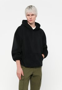 Zwarte fleece hoodie met een grote voorkantzak, lange mouwen en een capuchon met trekkoord, gecombineerd met olijfgroene cargobroeken.