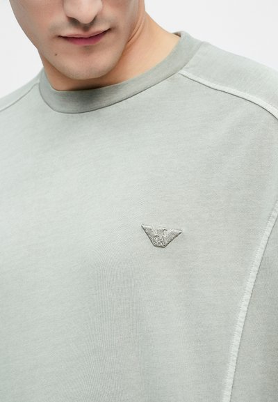 Φωτεινό γκρι φούτερ με ριμπ λαιμόκοψη, με μικρό κεντημένο λογότυπο αετού στο αριστερό στήθος και εμφανείς λεπτομέρειες ραφής.