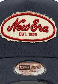 Ρουά ρυθμιζόμενο καπέλο με ξεφτισμένο μπεζ κομματάκι που φέρει κόκκινο κείμενο "New Era" και ετικέτα "EST. 1920". Λείο ύφασμα, δομημένος σχεδιασμός.