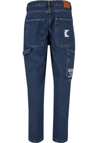 Denimske cargo hlače v temno modri barvi z več žepi, usnjenim oznako na pasu in kontrastnim belim napisom na levem žepu.