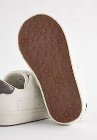 Baltas sporta apavi ar gludu ādas augstdaļu, ar pelēku metālisku akcentu. Gumijas zole ir brūnā krāsā un ar zvaigžņu rakstu.