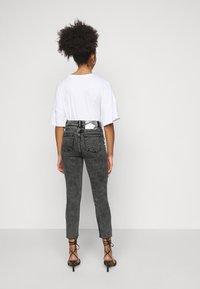 Vaqueros negros de talle alto con acabado texturizado, forma ajustada y dobladillo deshilachado, combinados con una camiseta blanca de corte holgado y tacones con tiras.