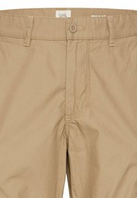 Beige bomuldsbukser med knaplukning, normal pasform, synlige stikninger og sidelommer. Stoffet ser let og tekstureret ud.