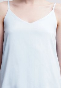 Top de tirantes finos y ajustables en color azul claro, con una textura suave y lisa y un diseño con escote en V.