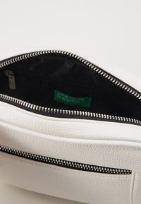 Borsa in pelle bianca texturizzata con una cerniera nera, dotata di una fodera interna nera e un'etichetta in tessuto verde con la scritta "UNITED COLORS OF BENETTON."