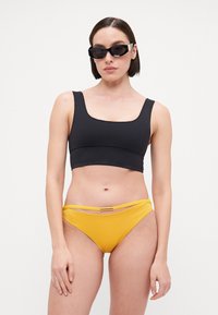Svart sporty bikinitopp med firkantet utrigning, kombinert med gule bikinitruser med et horisontalt bånd og metallisk detalj.