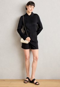 Černá košile s dlouhými rukávy, doplněná černými šortkami s vysokým pasem. Obsahuje malou krémovou crossbody tašku a černé sandály s blokovým podpatkem.