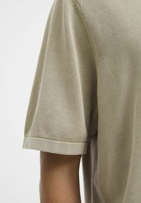 Korte mouwen beige gebreide shirt heeft een soepele textuur, een losse pasvorm en omgeslagen mouwen, met zichtbare stiksels langs de naden.