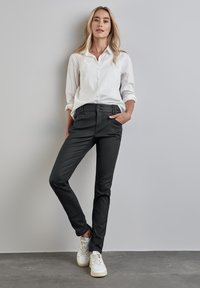 Svarta skräddarsydda byxor med två framskjutna fickor, matchade med en vit skjorta med knappar och vita sneakers. Slät textur och slim fit-design.