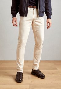 Pantalones de corte Slim en color beige, fabricados en algodón, con una textura suave. Combinados con zapatos de cuero marrón oscuro que presentan un diseño sencillo y un ligero detalle de costura.