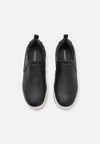 Sapatos slip-on pretos feitos de couro liso, com bico arredondado e sola branca, apresentando painéis laterais elásticos para facilitar o calce.