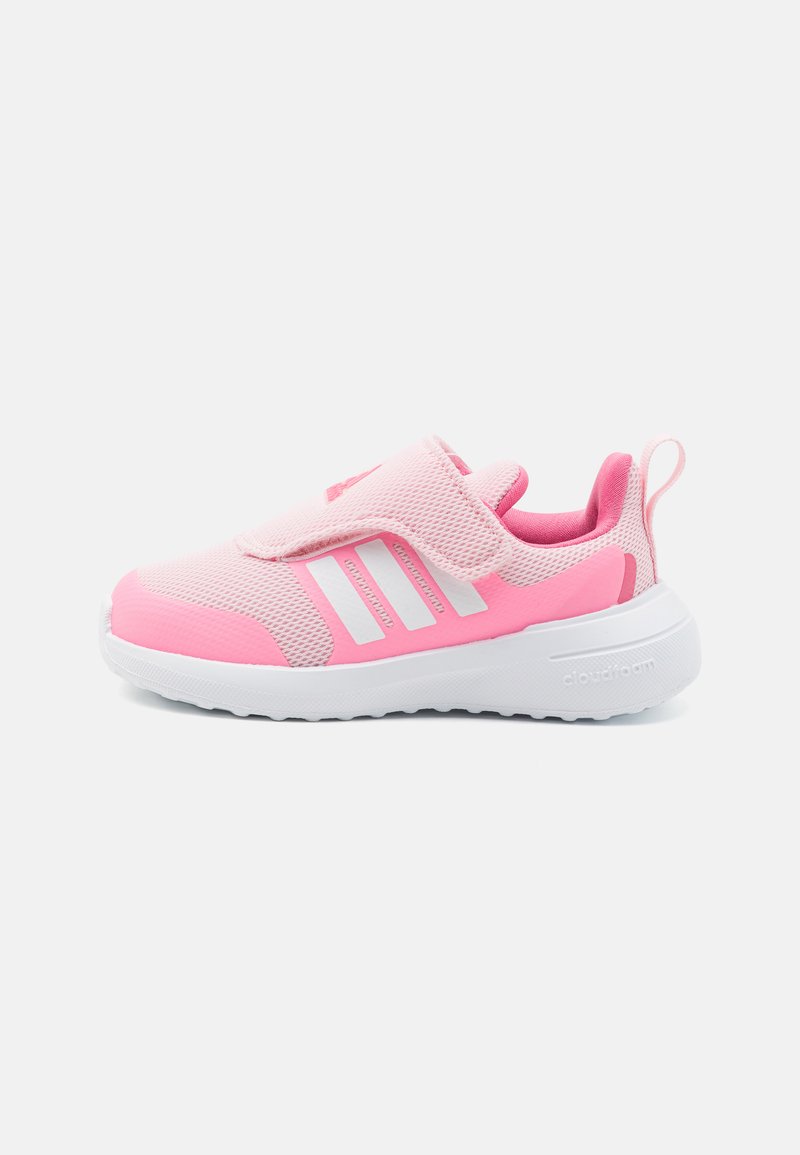 Scarpe da ginnastica rosa con tomaia in rete, fascia elastica e suola bianca. Progettate con tre righe bianche e un tab di estrazione testurizzato sul tallone.