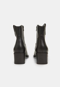 Botas de tobillo de cuero negro con tacón cuadrado, cierre de cremallera y textura lisa; cuentan con un diseño elegante y una silueta estructurada.