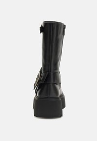 Stivali neri in pelle fino al ginocchio con suola piatta chunky, zip laterale e cinturino regolabile con dettagli in metallo.