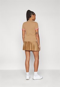 Ljusbrun stickad polodress med veckad kjol, korta ärmar med rosa detaljer, strukturerat mönster och figursydda överdel, matchad med vita sneakers.